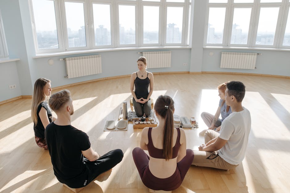 A diverse group of adults meditating in a spacious, sunlit studio with city views
